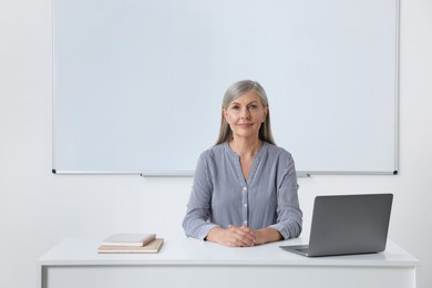 Professor sitting near laptop at desk in classroom, space for text
