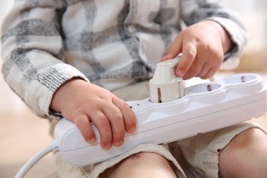 Little child playing with power strip and plug on floor indoors, closeup. Dangerous situation