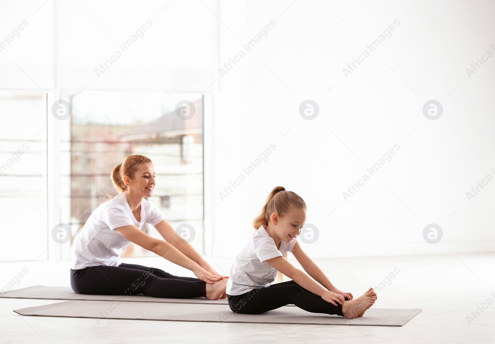 Photo of Mother and daughter in matching sportswear doing yoga together at home