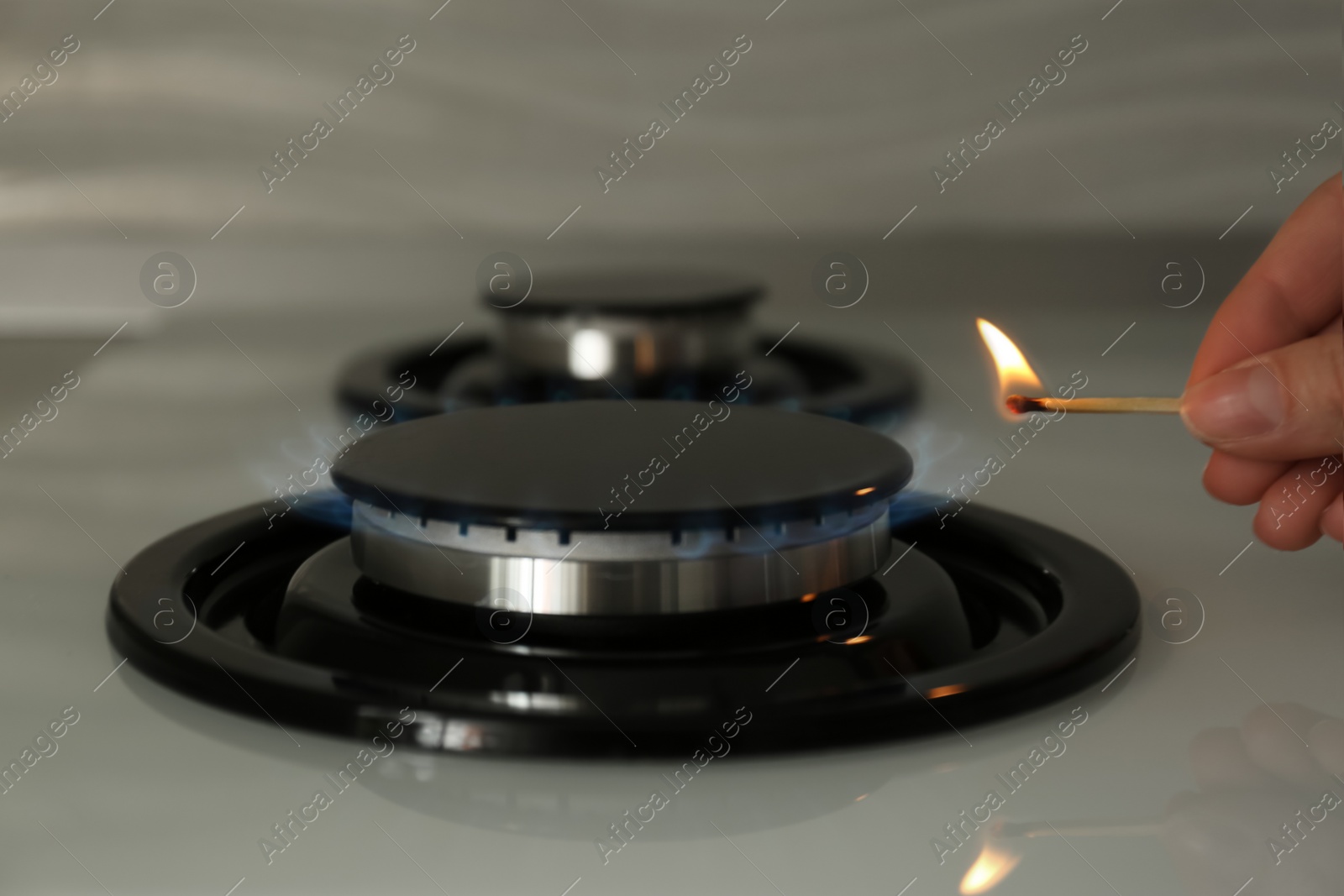 Photo of Woman lighting gas stove with match, closeup