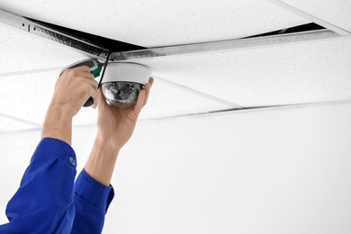 Technician installing CCTV camera on ceiling indoors, closeup