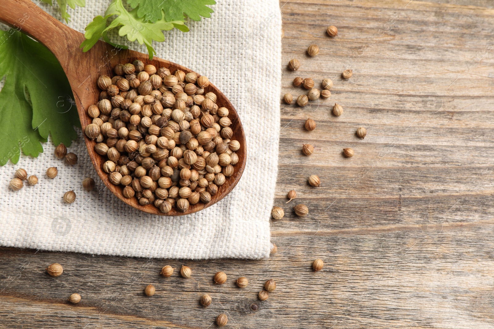 Photo of Spoon with dried coriander seeds and green leaves on wooden table, top view. Space for text