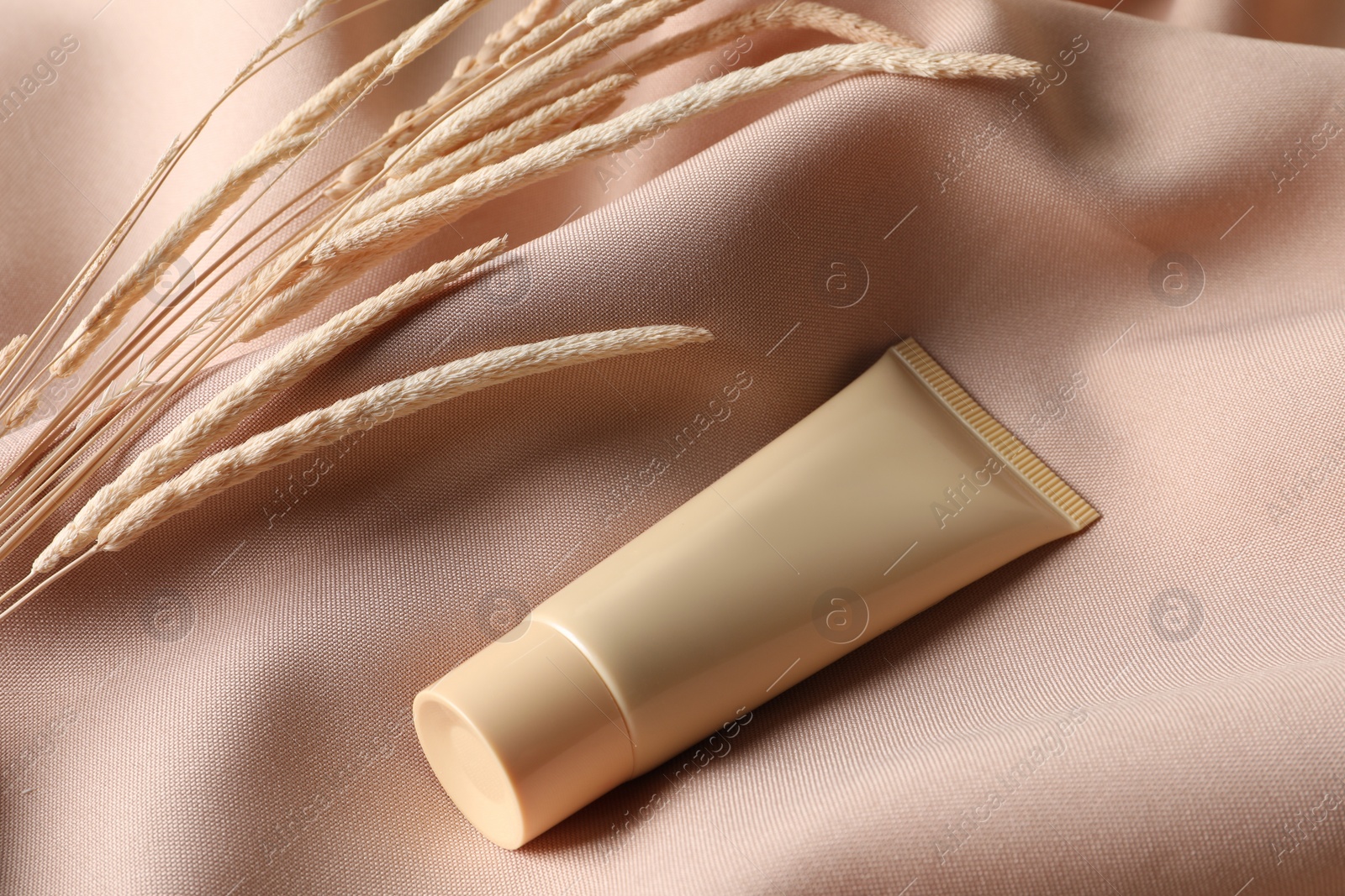 Photo of Tube of skin foundation and decorative plants on beige fabric. Makeup product