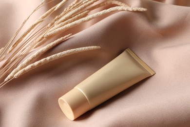 Tube of skin foundation and decorative plants on beige fabric. Makeup product