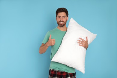 Photo of Smiling handsome man showing thumb up and holding soft pillow on light blue background