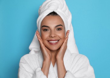 Photo of Beautiful young woman wearing bathrobe and towel on head against light blue background
