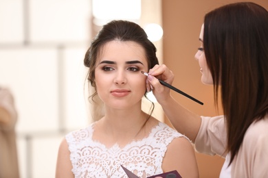 Photo of Professional makeup artist working with young bride in salon