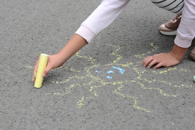 Photo of Little child drawing sun with chalk on asphalt, closeup