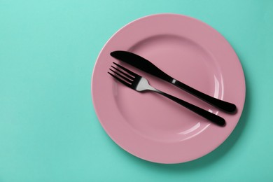 Pink ceramic plate and cutlery on turquoise background, top view. Space for text