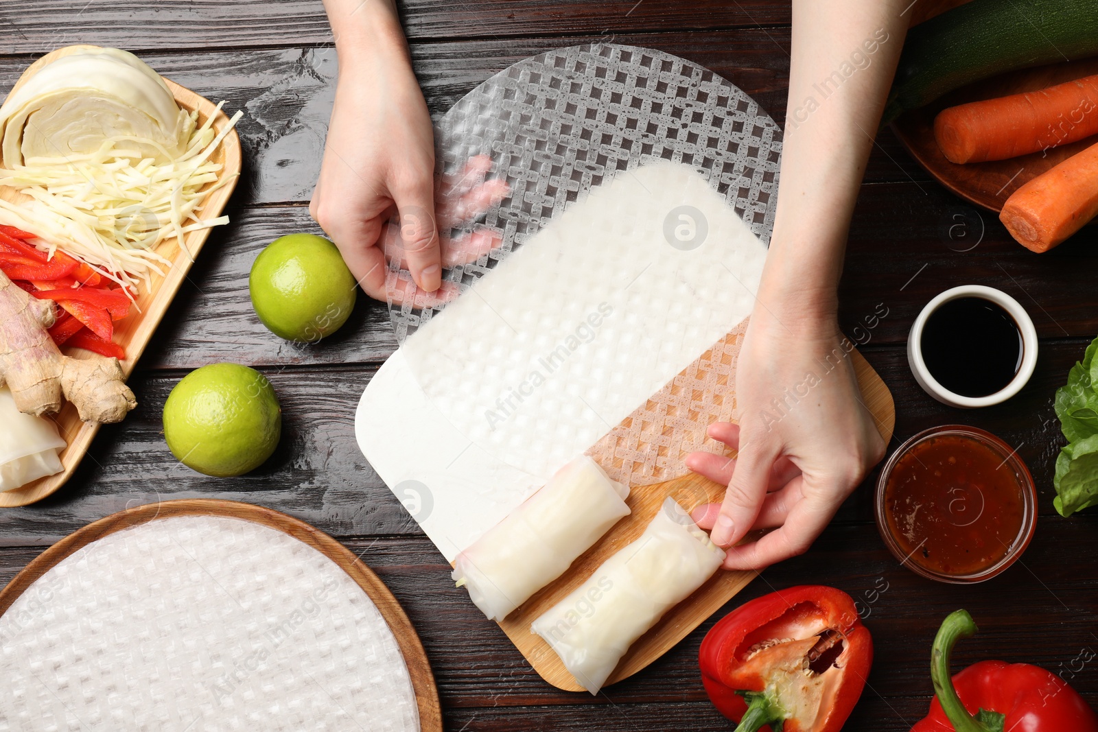 Photo of Making delicious spring rolls. Woman with fresh rice paper at wooden table, flat lay