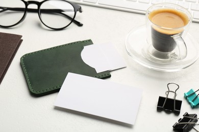 Photo of Leather business card holder with blank cards, glasses, coffee and stationery on white table