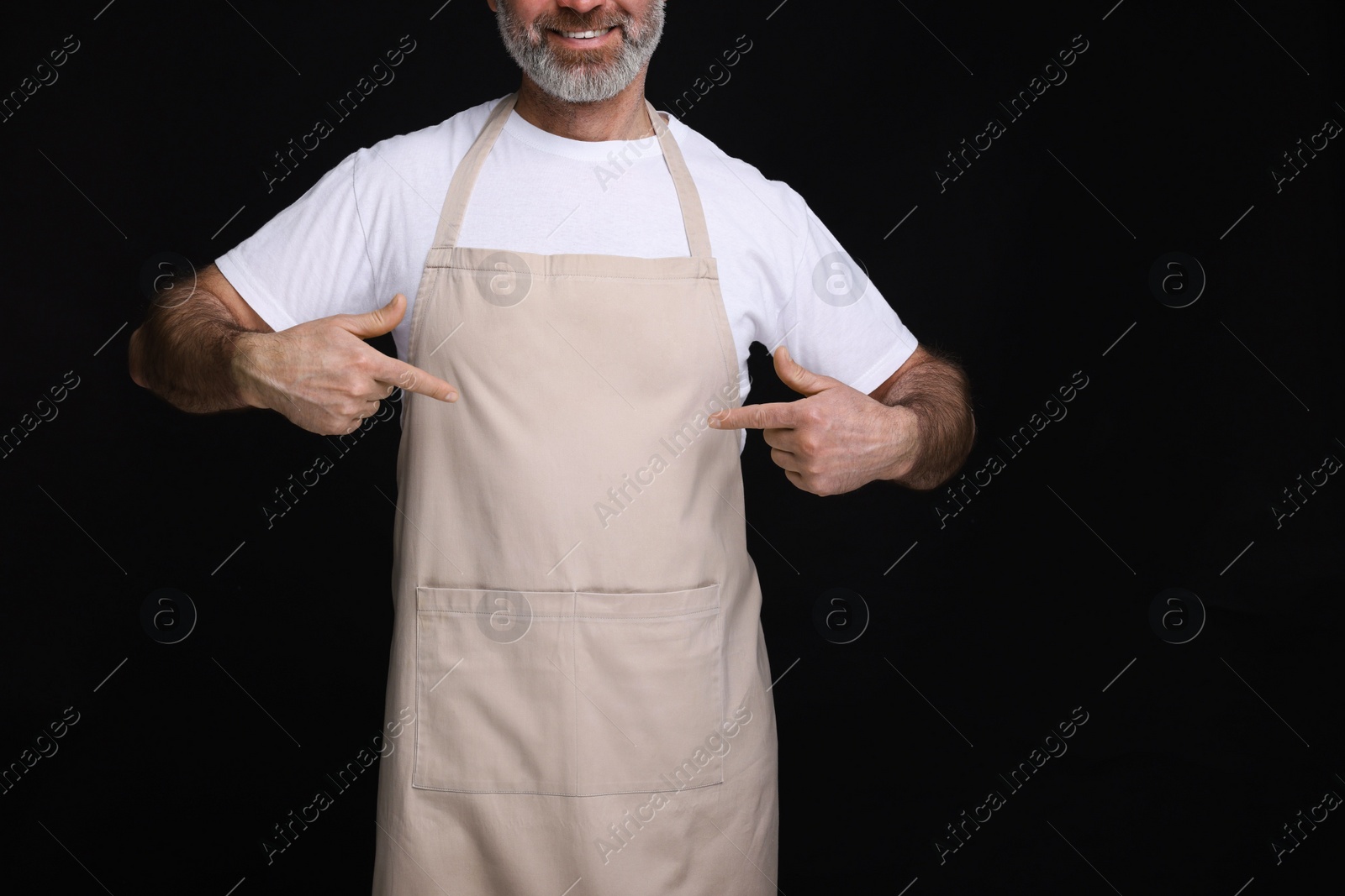 Photo of Man pointing at kitchen apron on black background, closeup. Mockup for design