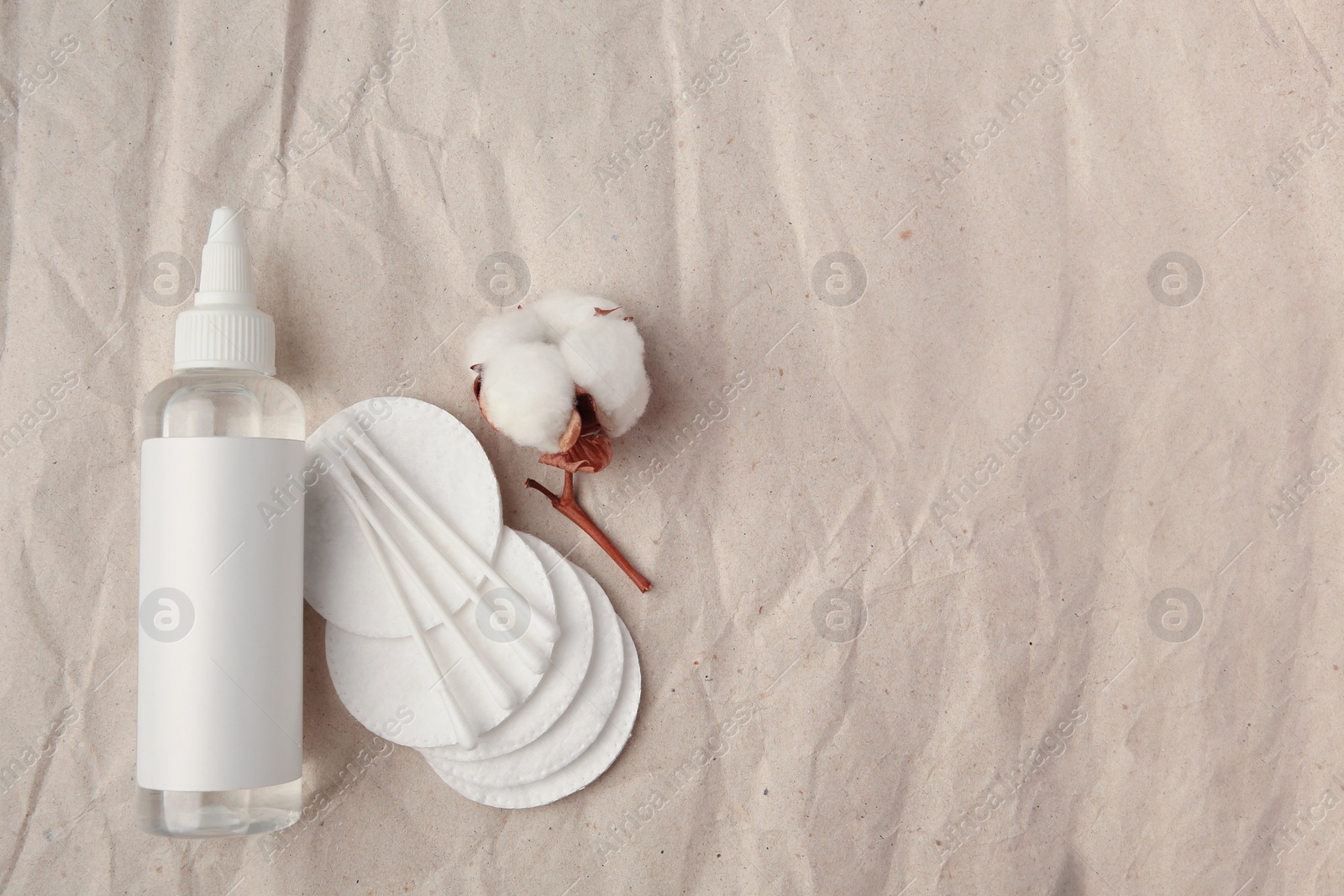 Photo of Flat lay composition with makeup remover and cotton flower on crumpled paper, space for text