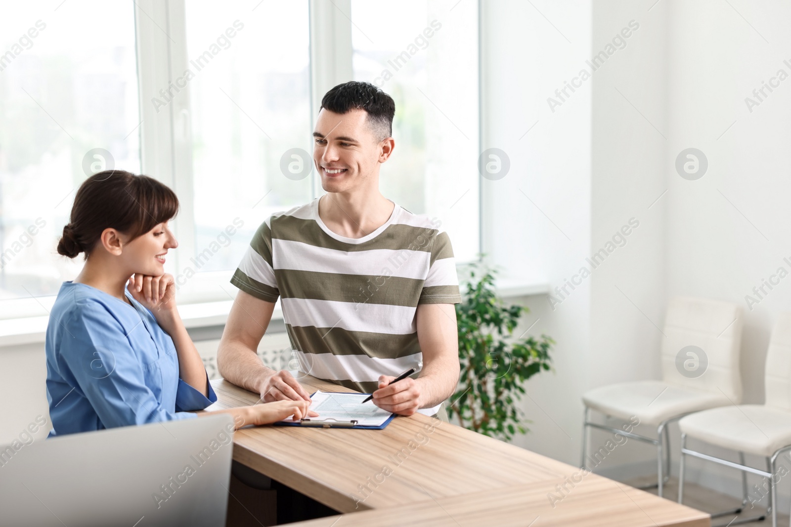 Photo of Smiling medical assistant working with patient at hospital reception. Space for text