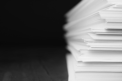 Photo of Stack of blank paper on grey stone table against dark background. Space for text