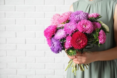 Woman holding bouquet of beautiful aster flowers against white brick wall, closeup. Space for text