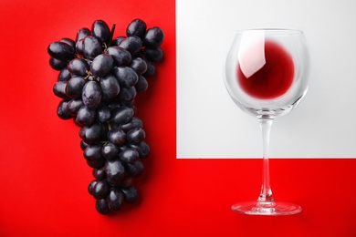 Photo of Glass with red wine and fresh ripe juicy grapes on color background, top view