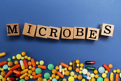 Photo of Word Microbes made with wooden cubes and colorful pills on blue background, flat lay