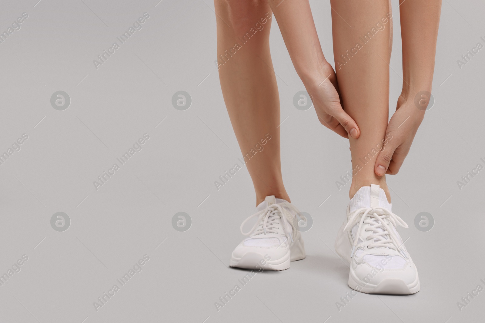 Photo of Woman suffering from leg pain on grey background, closeup. Space for text