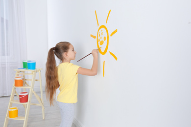 Photo of Little child painting sun on white wall indoors