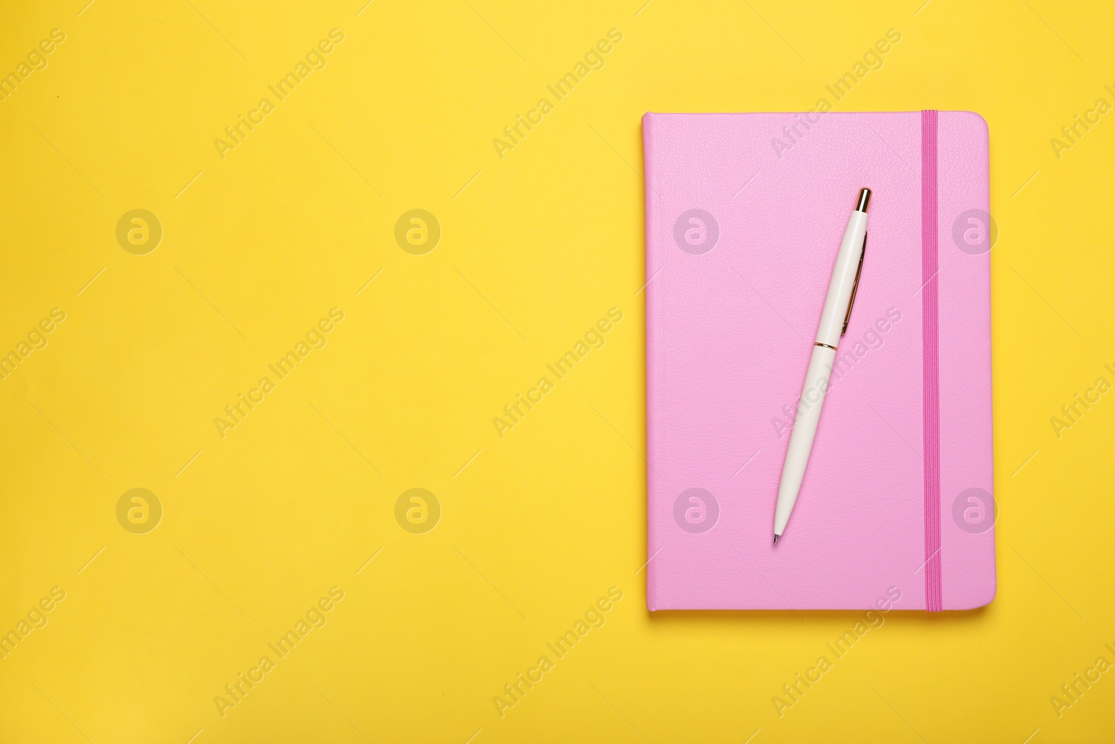 Photo of Closed pink notebook and pen on yellow background, top view. Space for text