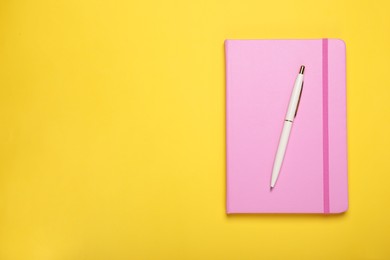 Photo of Closed pink notebook and pen on yellow background, top view. Space for text