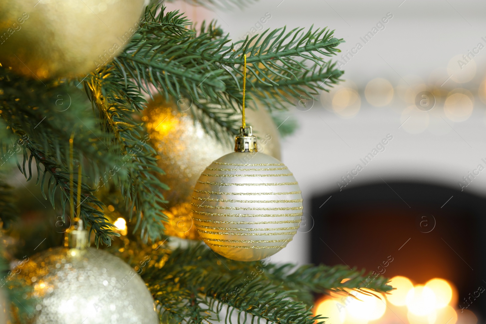 Photo of Beautiful golden Christmas balls hanging on fir tree branch against blurred background, closeup