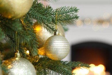 Photo of Beautiful golden Christmas balls hanging on fir tree branch against blurred background, closeup