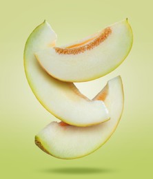 Image of Delicious ripe melon slices falling on light green background