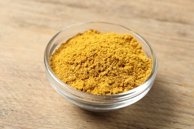 Photo of Curry powder in bowl on wooden table, closeup