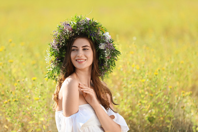 Young woman wearing wreath made of beautiful flowers in field on sunny day