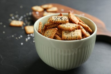 Photo of Delicious crispy crackers in bowl on black table, closeup