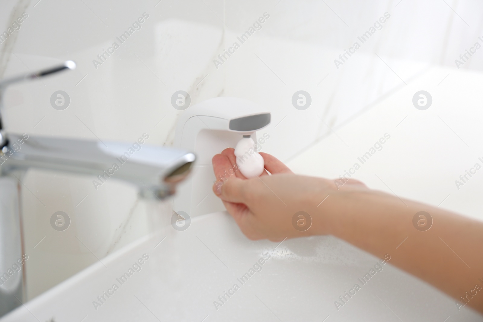 Photo of Woman using automatic soap dispenser in bathroom, closeup