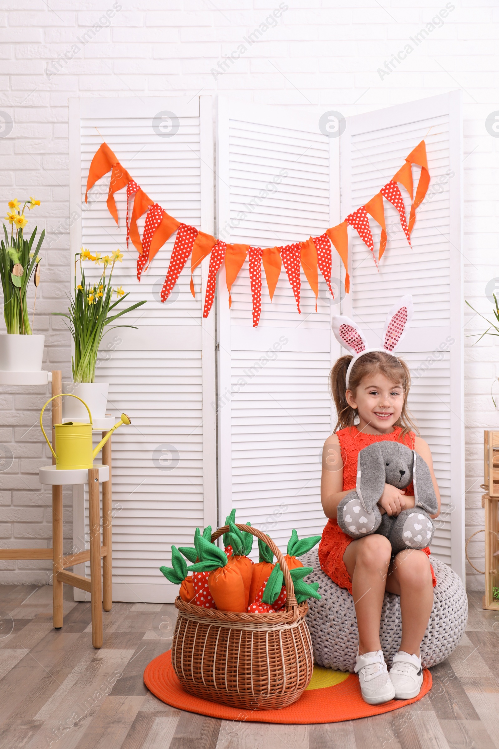 Photo of Adorable little girl with bunny ears, toy rabbit and carrots in Easter photo zone