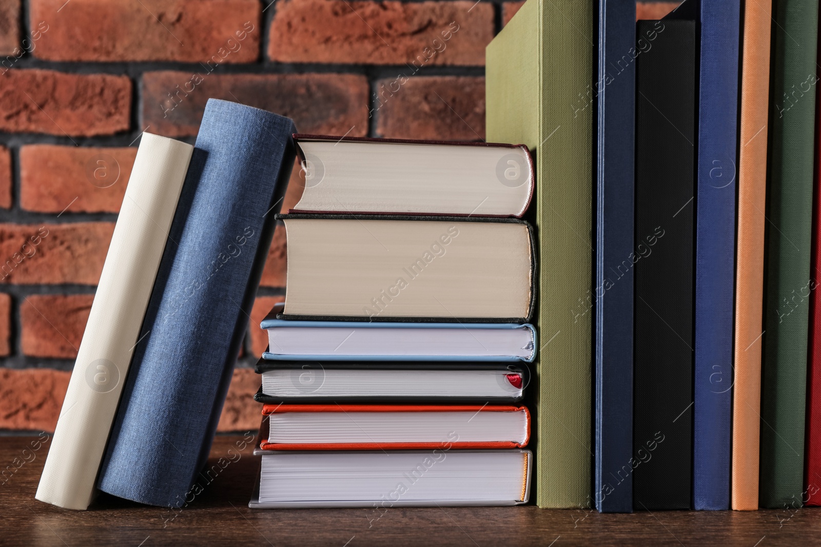 Photo of Many hardcover books on wooden table near brick wall