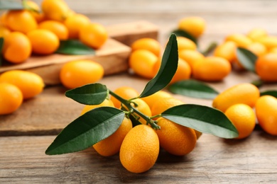 Fresh ripe kumquats and leaves on wooden table, closeup