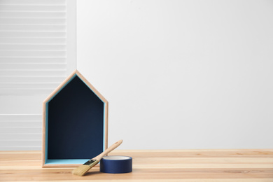 Photo of House shaped shelf and decorator tools on table indoors. Space for text