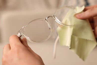 Woman cleaning glasses with microfiber cloth at home, closeup