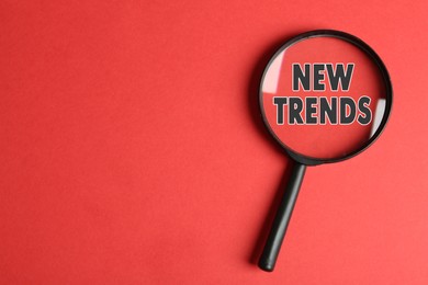 Image of Searching new and popular trends. Magnifying glass over words on red background, top view