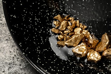Photo of Bowl with gold nuggets on grey table, closeup