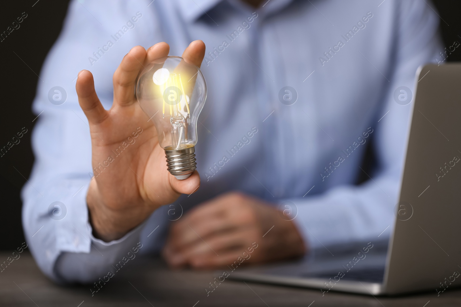 Photo of Glow up your ideas. Closeup view of man holding light bulb while working at wooden desk, space for text