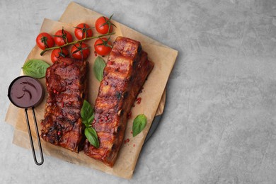 Photo of Tasty roasted pork ribs served with sauce, basil and tomatoes on grey table, top view. Space for text