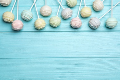 Photo of Sweet colorful cake pops on turquoise wooden background, flat lay. Space for text