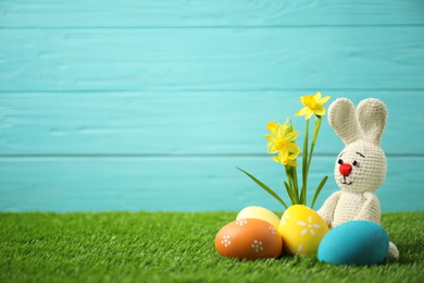 Colorful Easter eggs, rabbit and narcissus flowers in green grass against light blue background. Space for text