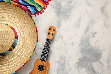 Photo of Mexican sombrero hat, guitar and colorful poncho on grey textured background, flat lay. Space for text