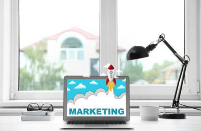 Image of Digital marketing concept. Modern laptop and lamp on table near window indoors