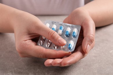 Photo of Woman taking pill out from blister pack at grey table, closeup