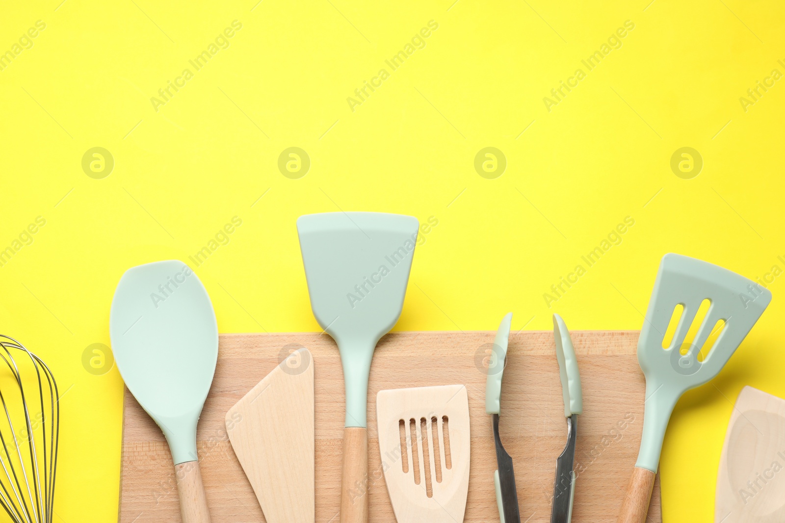 Photo of Different spatulas and tongs on yellow background, flat lay. Space for text