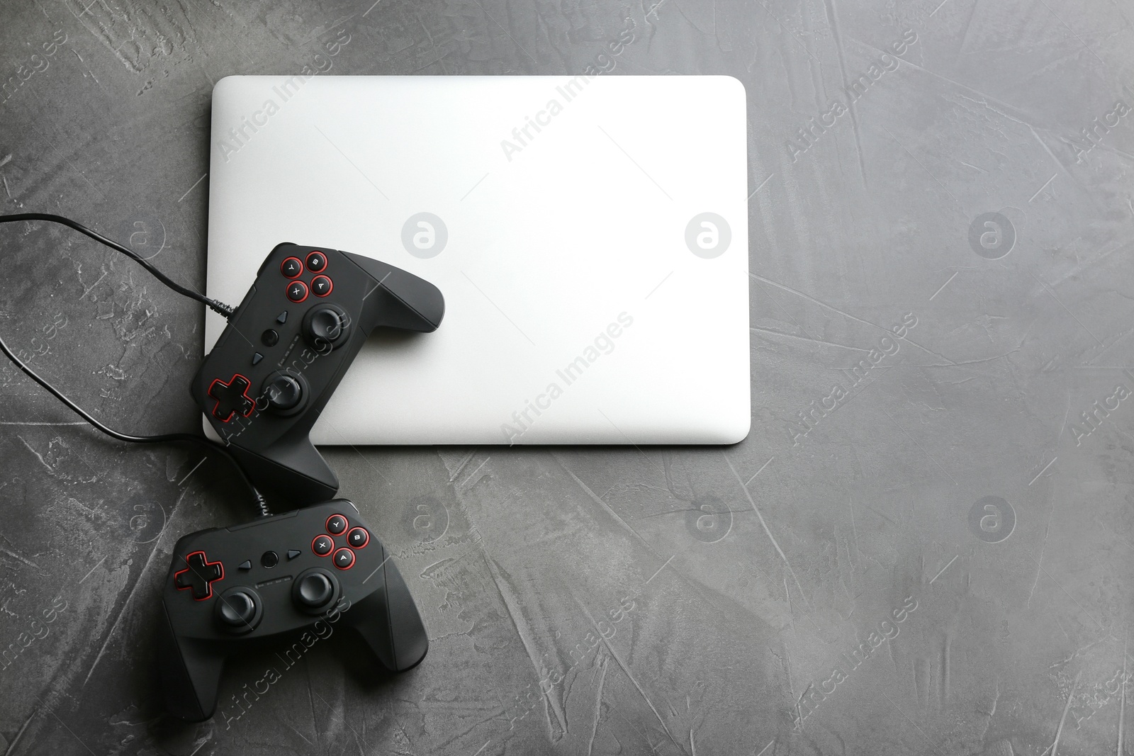 Photo of Video game controllers and laptop on grey background, top view with space for text