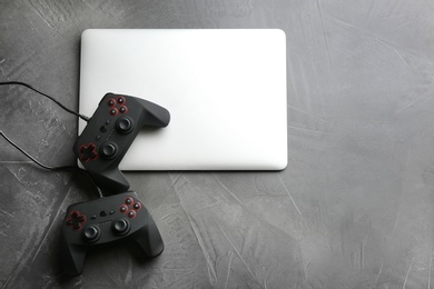 Video game controllers and laptop on grey background, top view with space for text